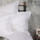 クラシック・ホテル仕様の大きめの枕を、白い無地、縁のデザインが特徴的なオックスフォード型ピローケースで仕上げたスタイリング例、クラシックで、ヨーロッパのブティックホテルのような雰囲気 | Beaumont & Brown