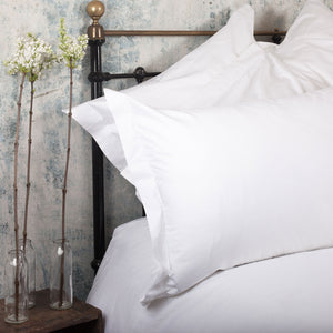 ホテル仕様の大きめの枕を、クラシックな白いリネンのピローケースで仕上げたスタイリング例、サイドテーブルにお花を飾れば、ヨーロッパのブティックホテルのような雰囲気に | Beaumont & Brown